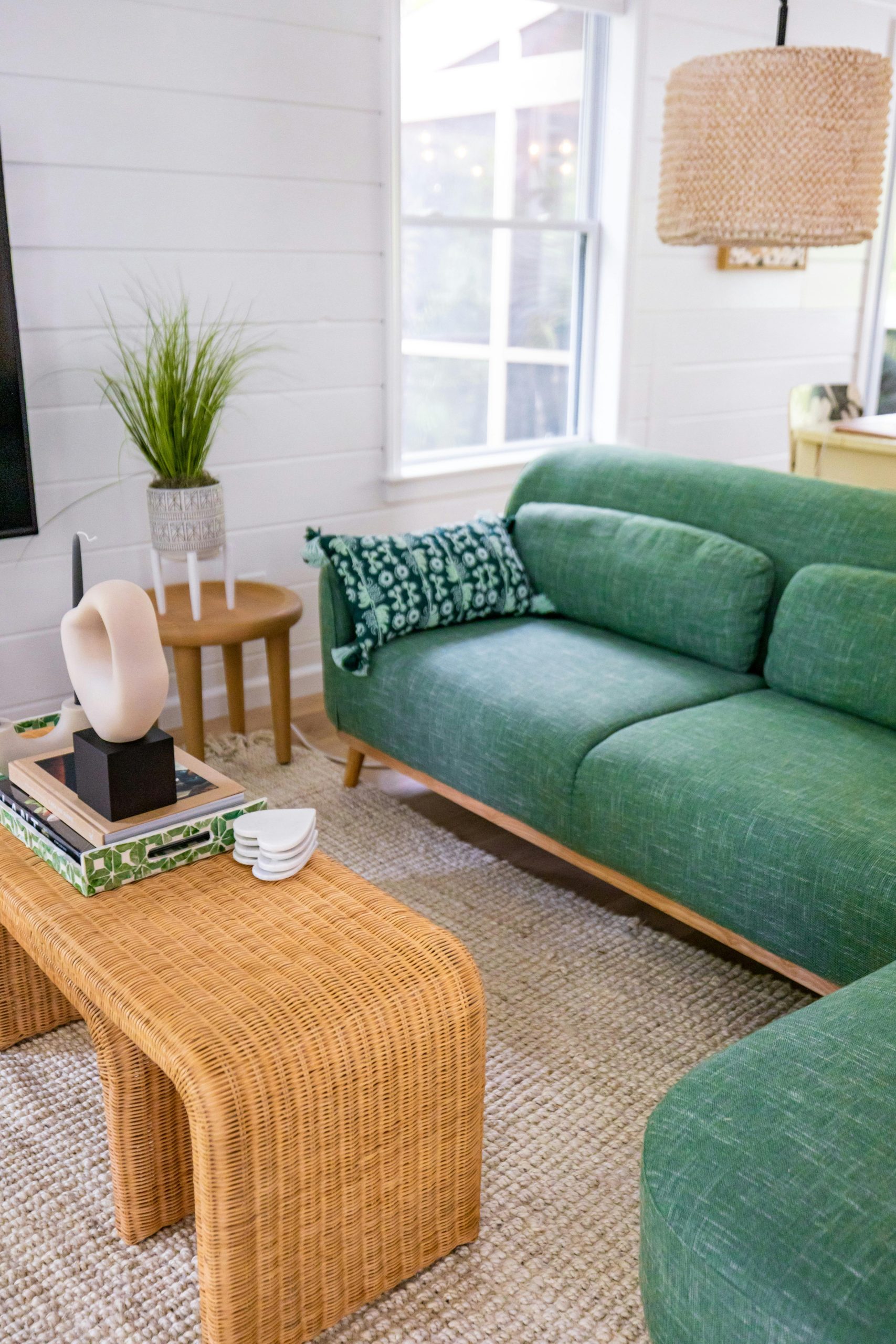 A stylish living room featuring a green sofa and rattan table, perfect for a relaxed home vibe.
