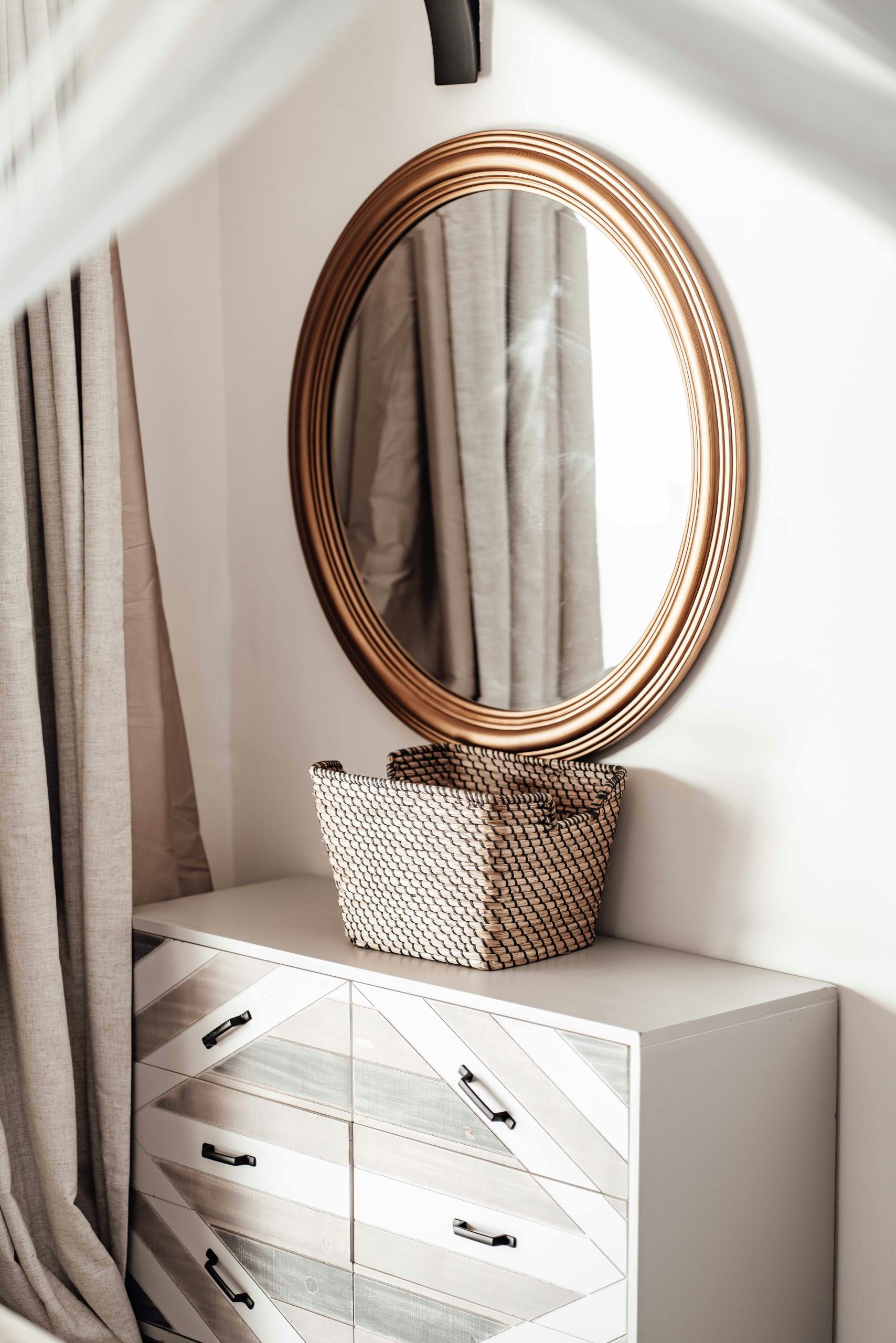 Stylish interior design featuring a round mirror, woven basket, and modern dresser in a cozy room.